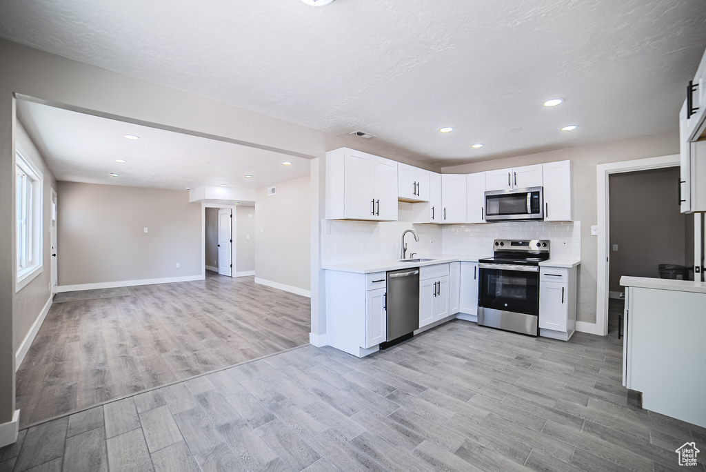 Kitchen featuring appliances with stainless steel finishes, tasteful backsplash, light countertops, light wood finished floors, and recessed lighting