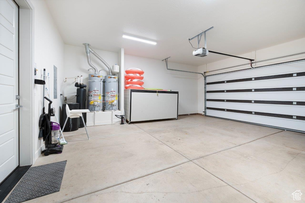 Garage with strapped water heater, refrigerator, and a garage door opener