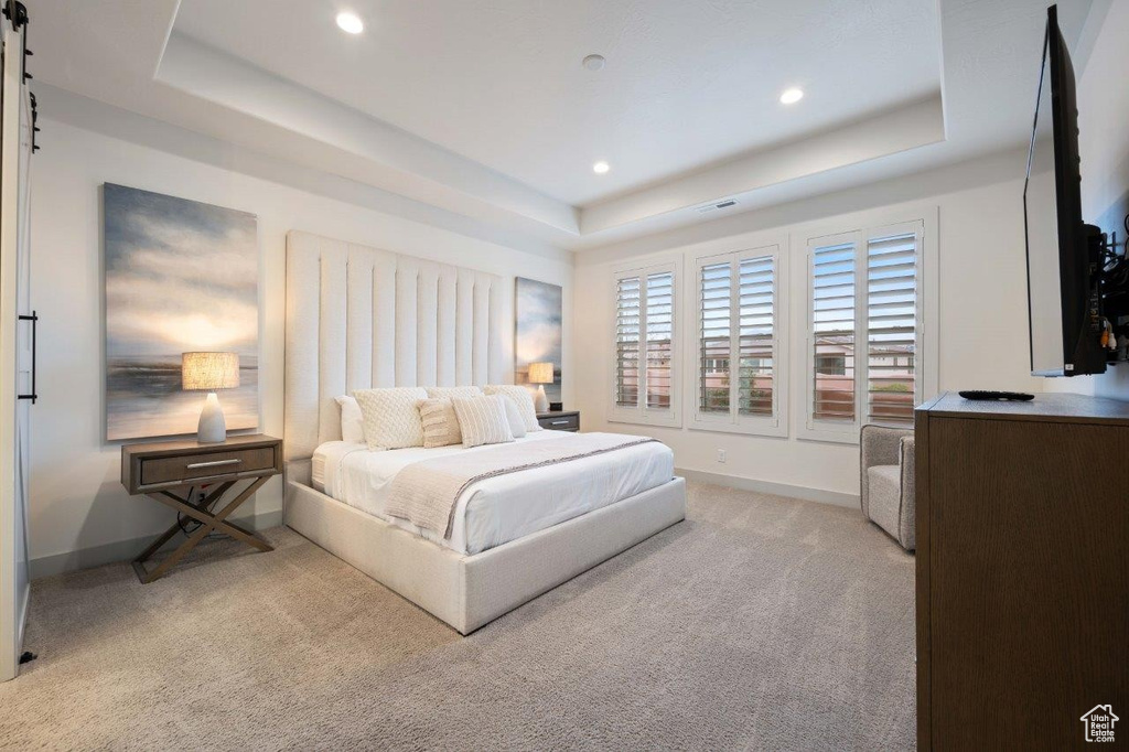 Bedroom featuring a raised ceiling, light colored carpet, recessed lighting, and a barn door