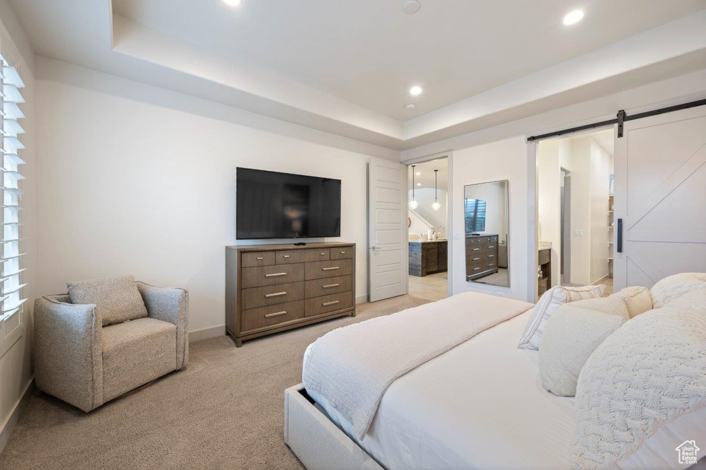 Bedroom with light colored carpet, a raised ceiling, ensuite bath, recessed lighting, and a barn door