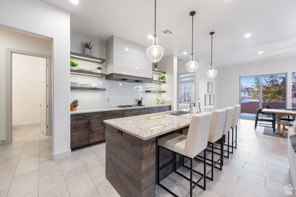 Kitchen with open shelves, tasteful backsplash, a kitchen bar, stainless steel gas cooktop, and dark brown cabinets
