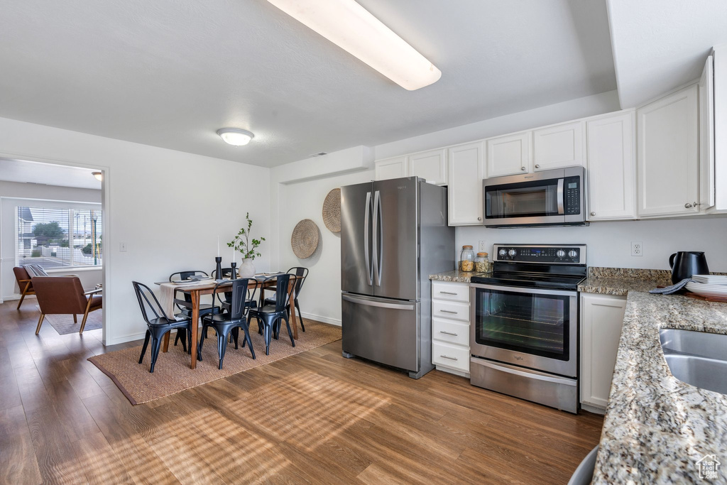 Kitchen with stainless steel appliances, wood finished floors, white cabinetry, and light stone countertops