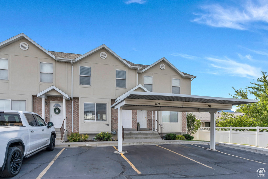 View of property featuring covered and uncovered parking, brick siding, and stucco siding