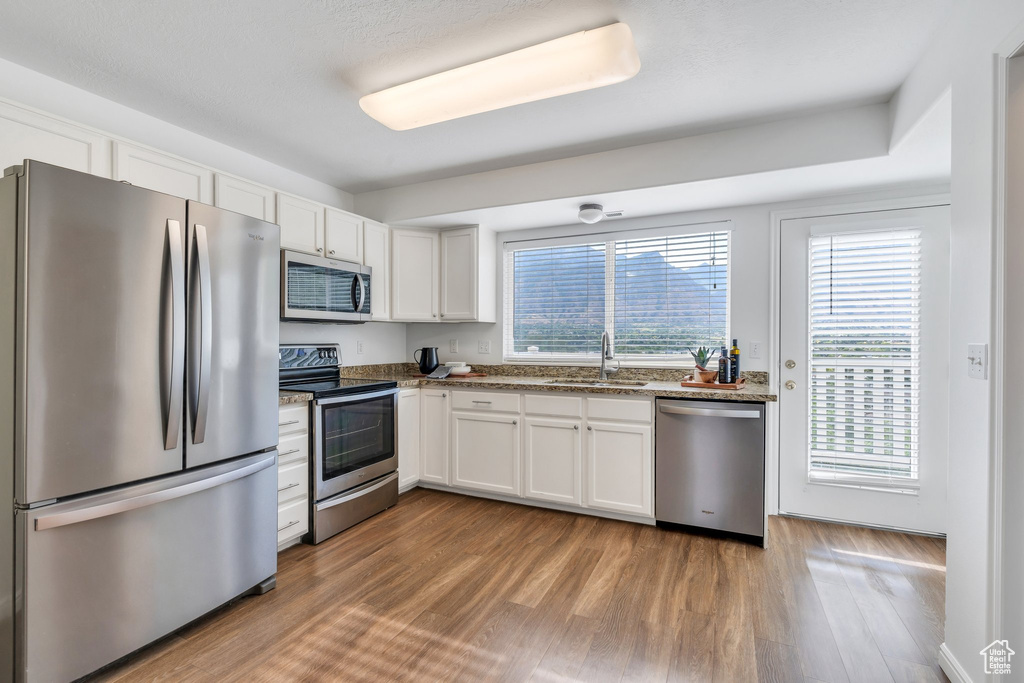 Kitchen featuring appliances with stainless steel finishes, white cabinetry, wood finished floors, and stone countertops