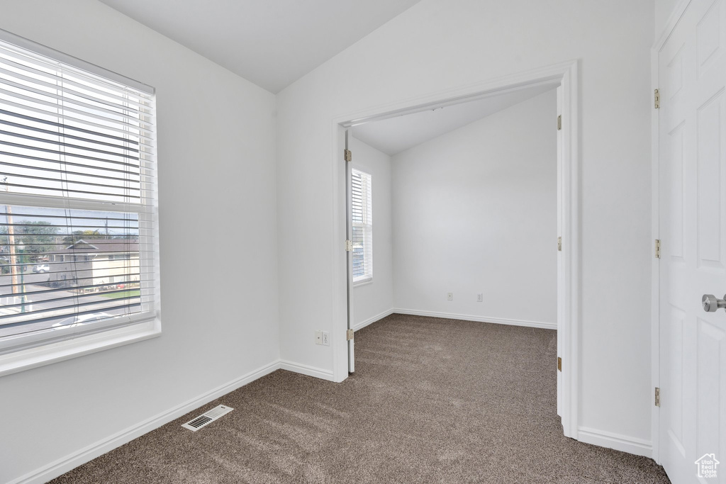Spare room featuring lofted ceiling and dark colored carpet