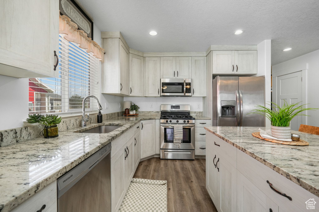 Kitchen with appliances with stainless steel finishes, dark wood-style flooring, light stone countertops, recessed lighting, and a textured ceiling