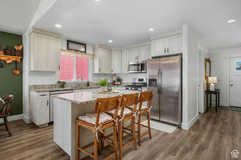 Kitchen featuring appliances with stainless steel finishes, wood finished floors, a breakfast bar, light stone countertops, and recessed lighting