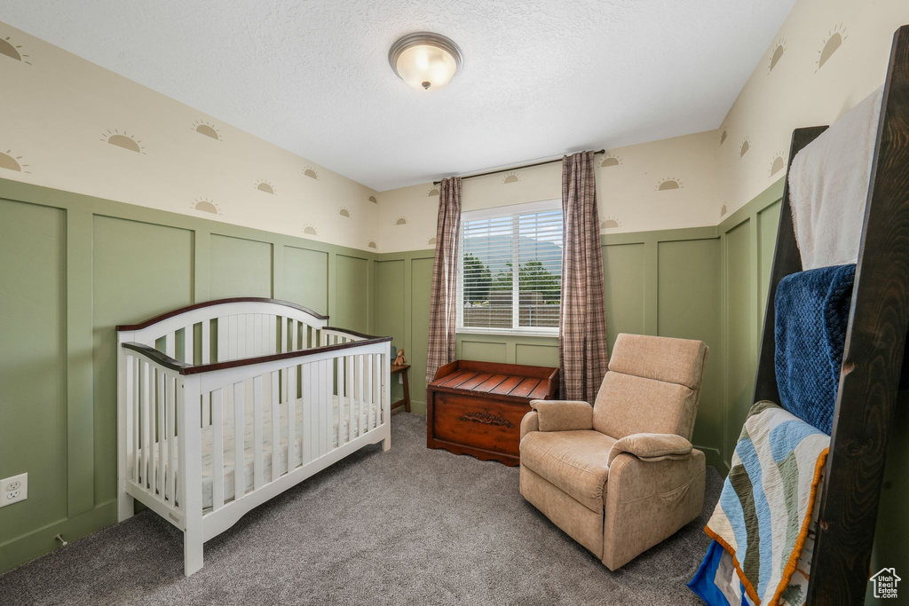 Bedroom with a decorative wall, carpet floors, a textured ceiling, and wainscoting