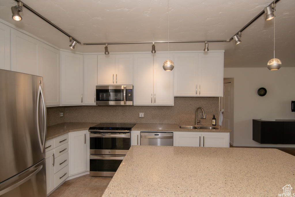 Kitchen with appliances with stainless steel finishes, backsplash, white cabinets, light stone counters, and rail lighting