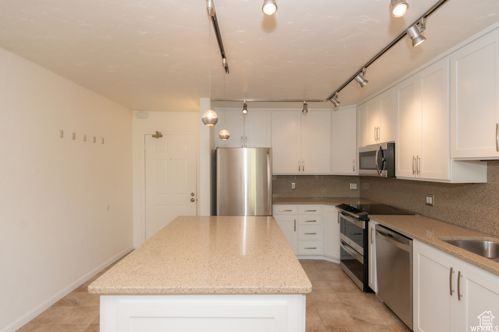 Kitchen with stainless steel appliances, a kitchen island, decorative backsplash, white cabinetry, and light stone countertops