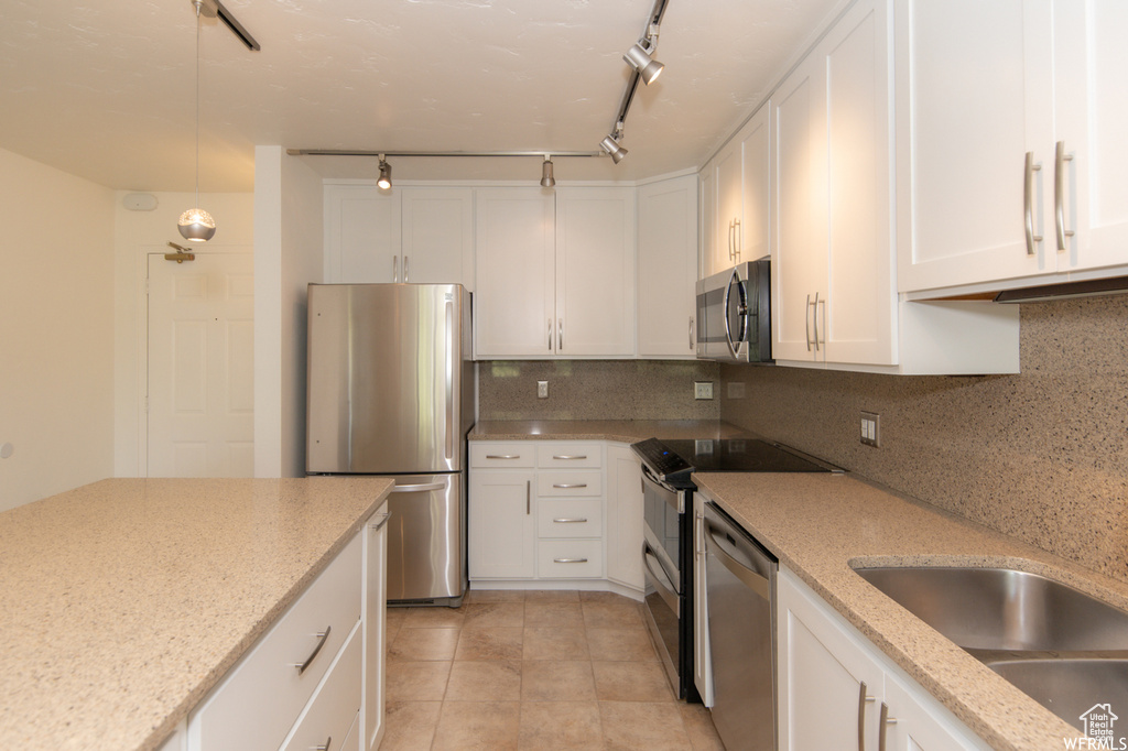 Kitchen featuring appliances with stainless steel finishes, white cabinets, backsplash, light stone countertops, and pendant lighting