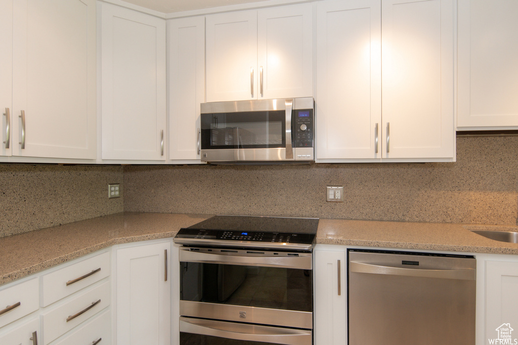 Kitchen featuring stainless steel appliances, backsplash, white cabinets, and light stone countertops