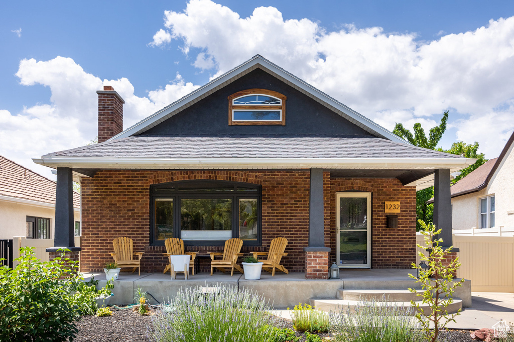 Rear view of house with covered porch, a chimney, brick siding, and a shingled roof