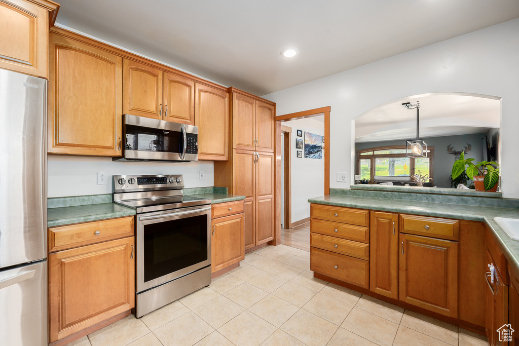 Kitchen with appliances with stainless steel finishes, arched walkways, recessed lighting, light tile patterned floors, and pendant lighting