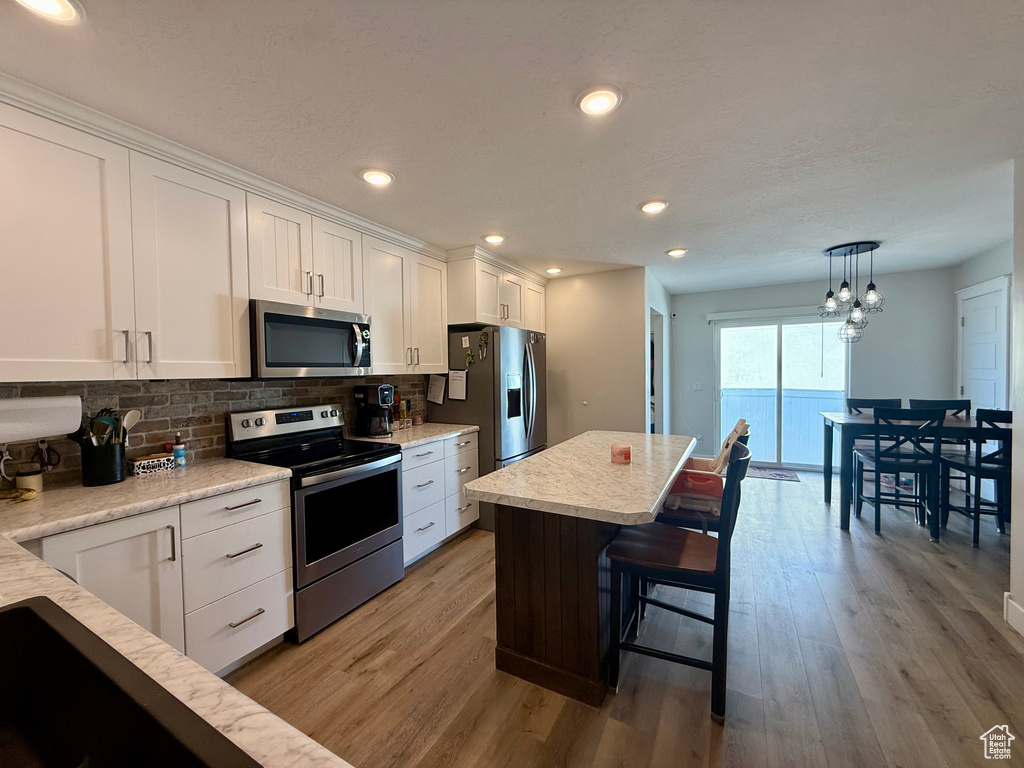 Kitchen featuring appliances with stainless steel finishes, white cabinets, wood finished floors, a breakfast bar, and recessed lighting