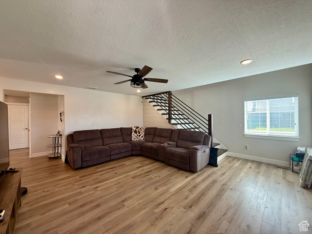 Living room featuring stairs, light wood-style floors, a textured ceiling, ceiling fan, and recessed lighting