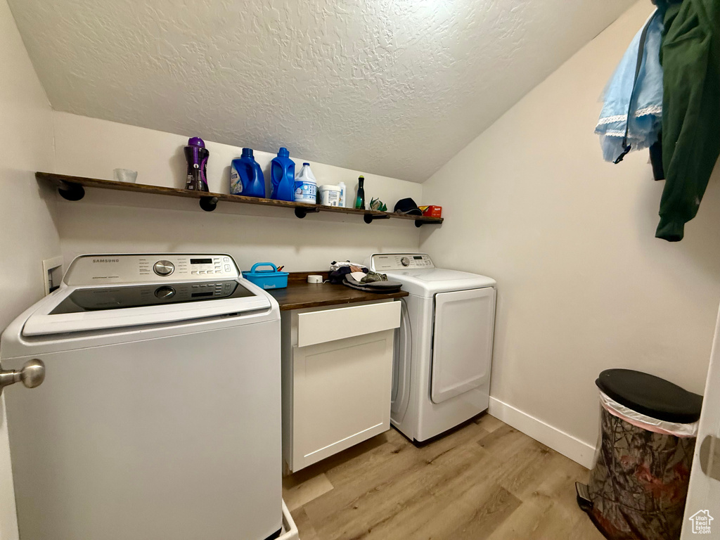 Washroom featuring light wood finished floors, a textured ceiling, and washer and dryer
