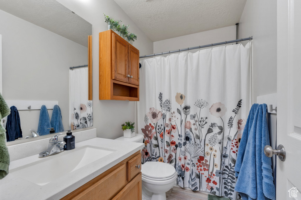 Full bathroom featuring vanity, a textured ceiling, curtained shower, and wood finished floors