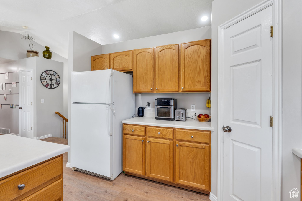 Kitchen with freestanding refrigerator, light wood-style flooring, light countertops, vaulted ceiling, and recessed lighting