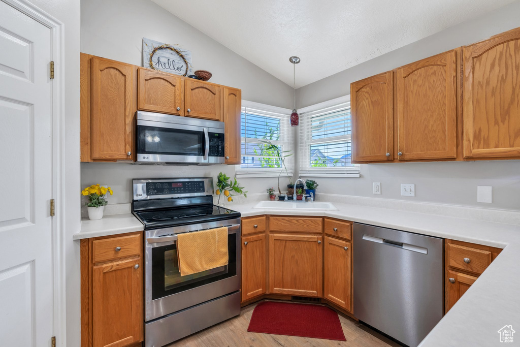 Kitchen with stainless steel appliances, vaulted ceiling, light countertops, light wood-style floors, and decorative light fixtures