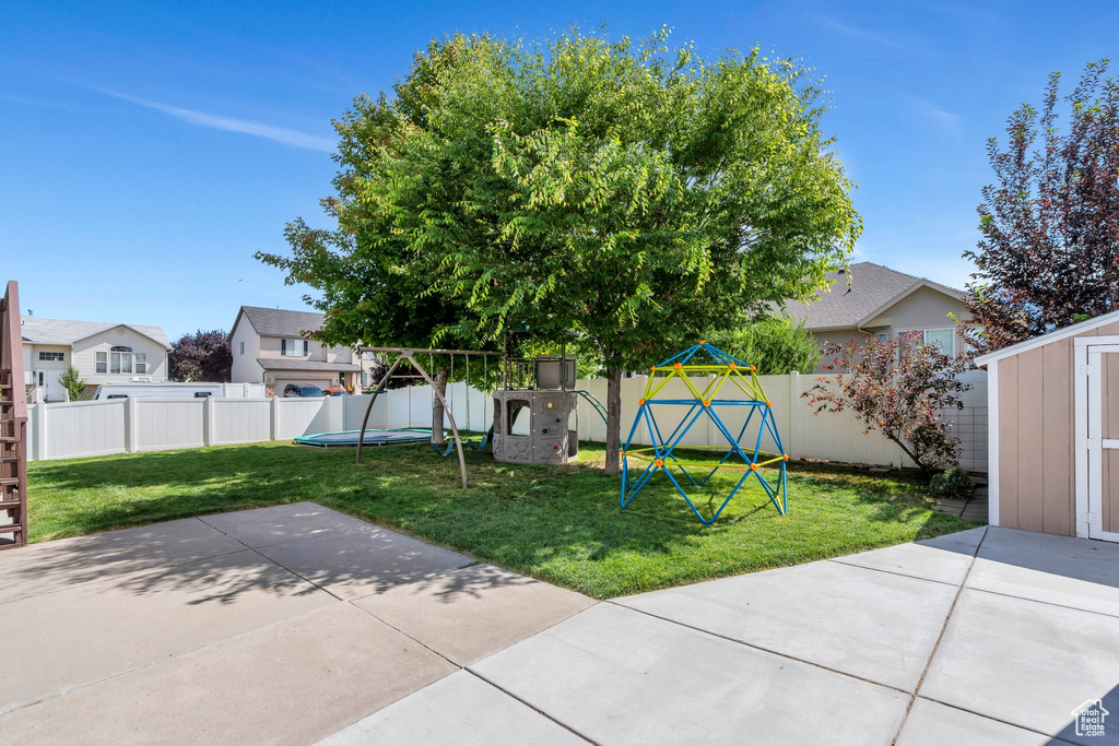 Fenced backyard with a playground, a patio, a storage unit, and a residential view