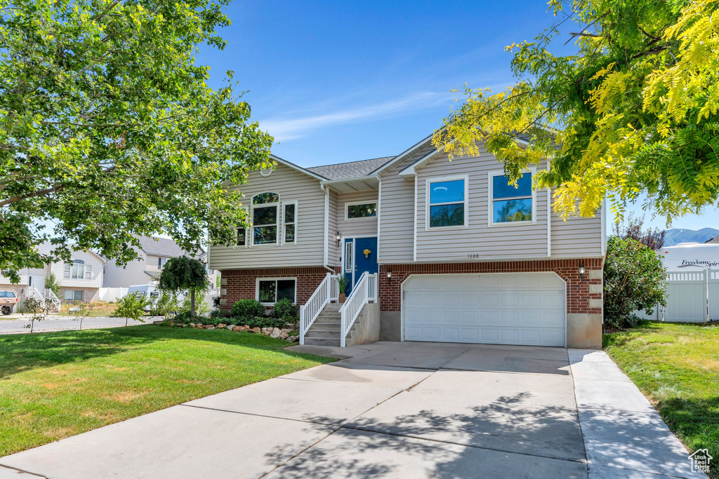 Bi-level home featuring an attached garage, concrete driveway, a front yard, and brick siding