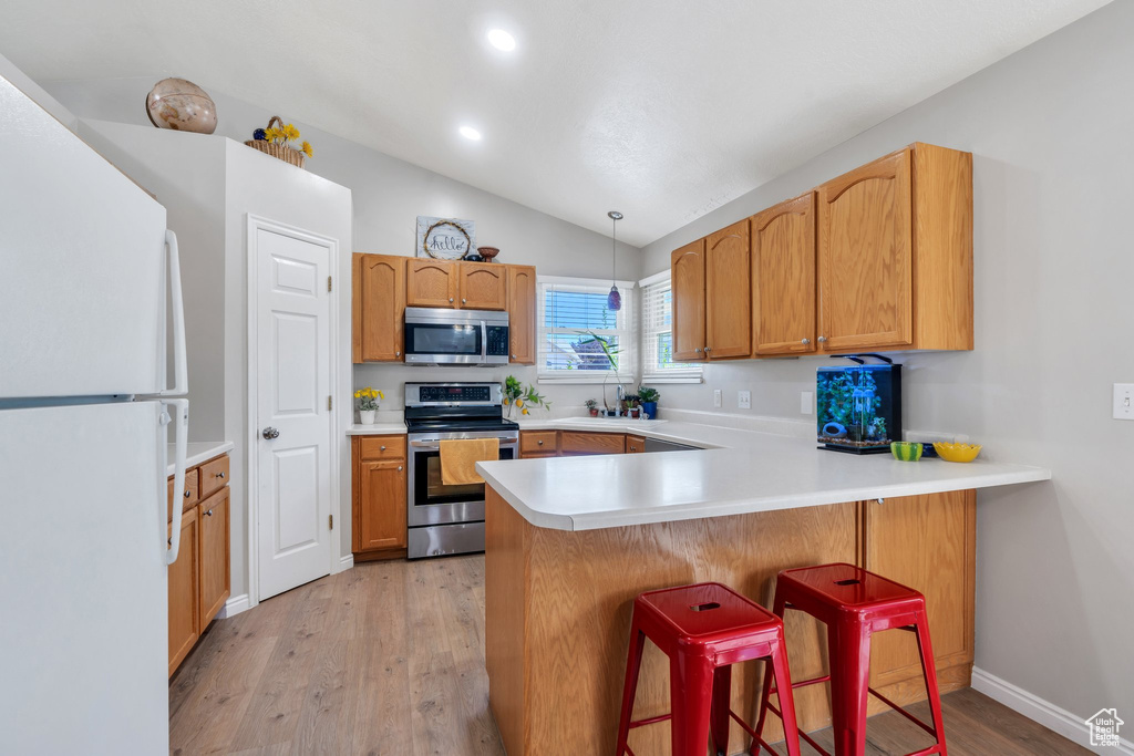 Kitchen with stainless steel appliances, lofted ceiling, a peninsula, light wood-type flooring, and a breakfast bar area