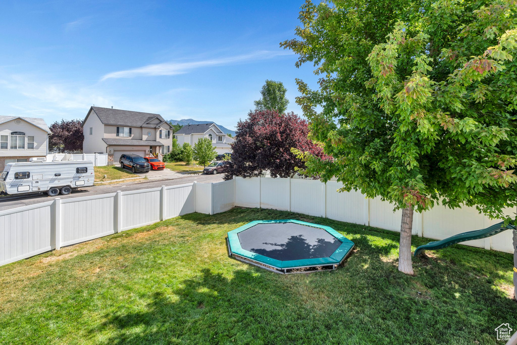 Fenced backyard featuring a trampoline and a residential view