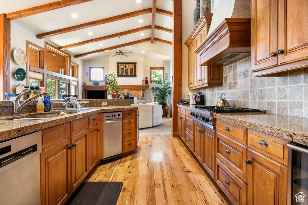 Kitchen with appliances with stainless steel finishes, wine cooler, custom exhaust hood, a fireplace, and light wood finished floors