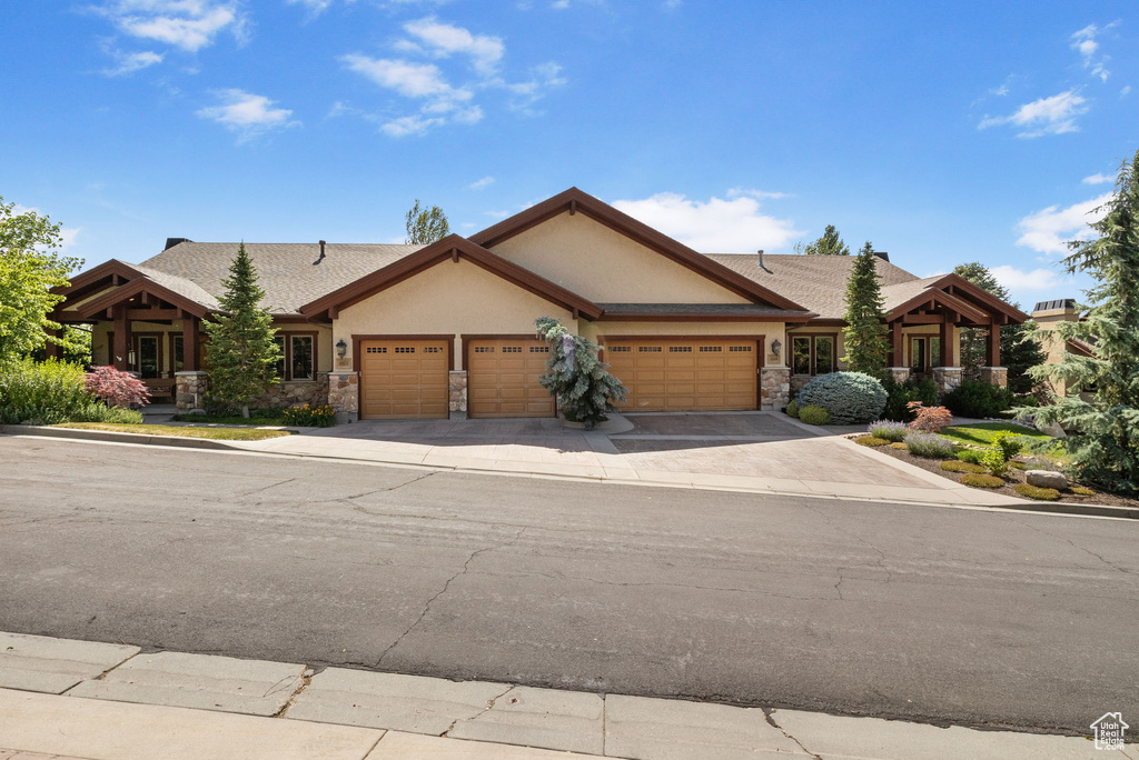 View of front of house featuring an attached garage, stucco siding, stone siding, and driveway