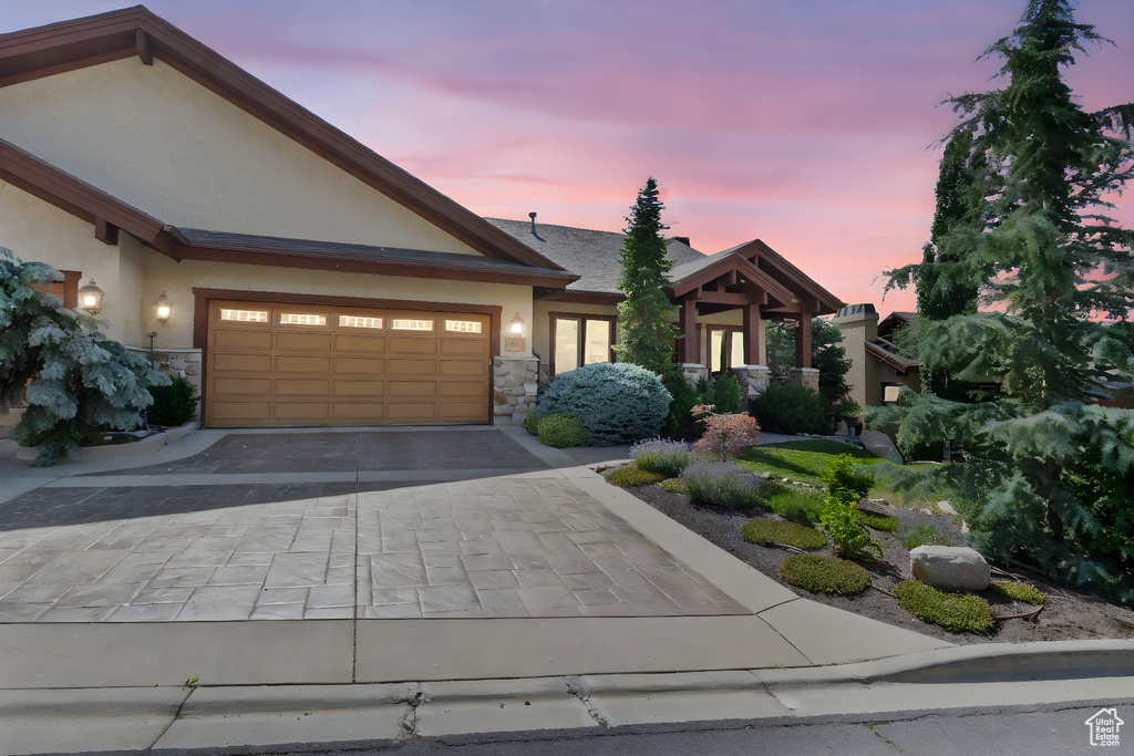 View of front of house featuring stone siding, stucco siding, decorative driveway, and a garage