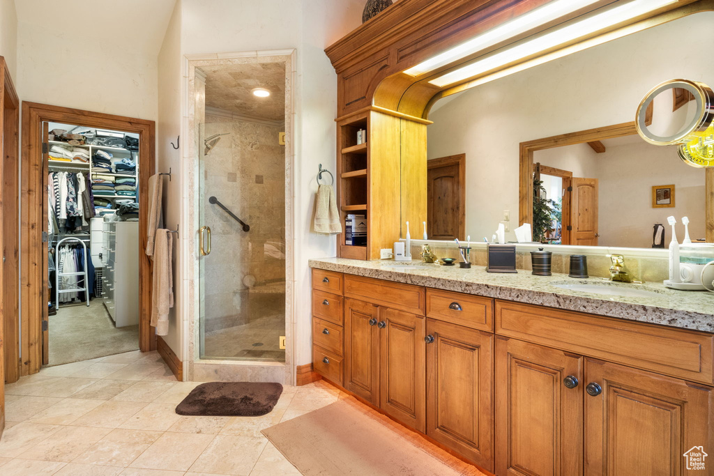 Bathroom featuring a shower stall, double vanity, a walk in closet, and tile patterned floors