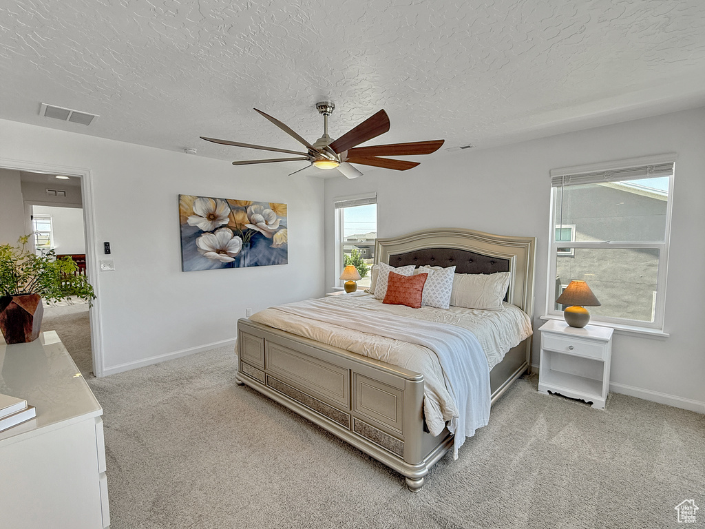 Bedroom featuring light colored carpet, multiple windows, a textured ceiling, and a ceiling fan