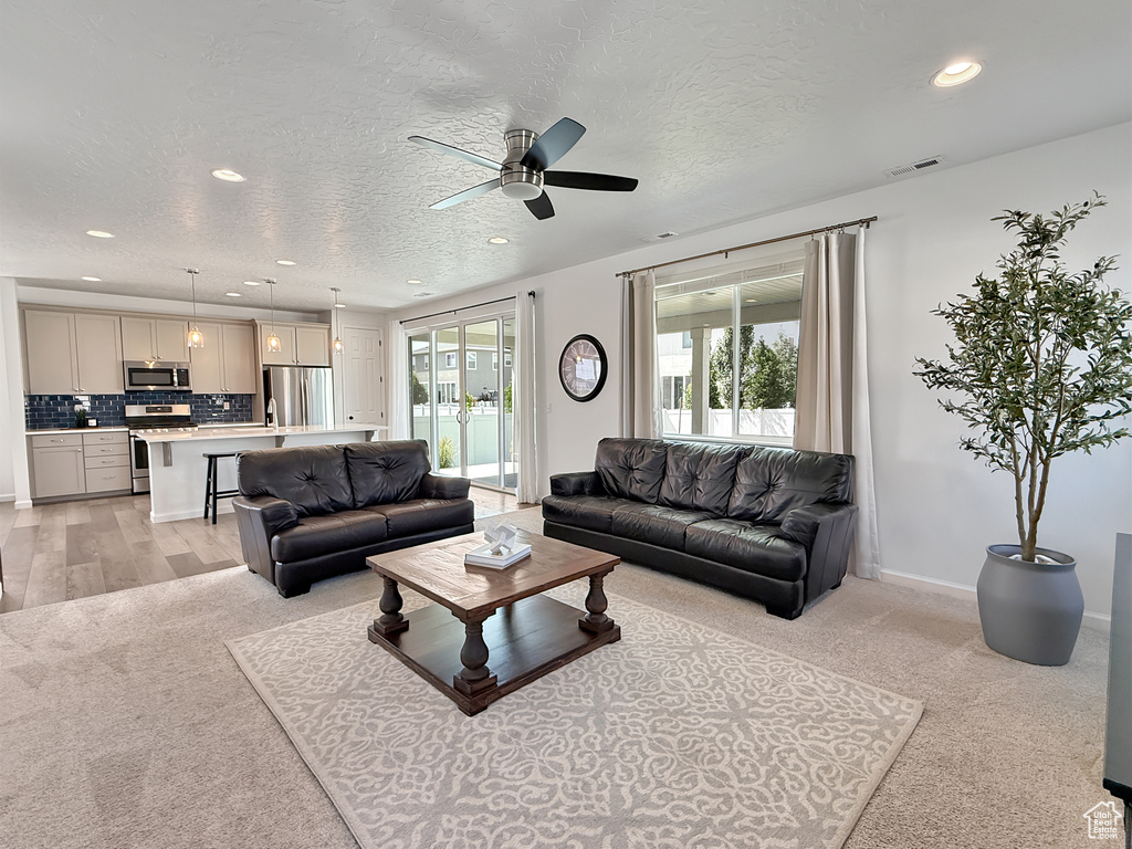 Living area with recessed lighting, a ceiling fan, a textured ceiling, and light colored carpet