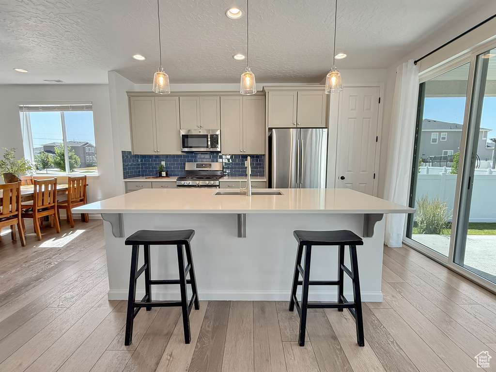 Kitchen featuring stainless steel appliances, a textured ceiling, light countertops, an island with sink, and light wood-type flooring