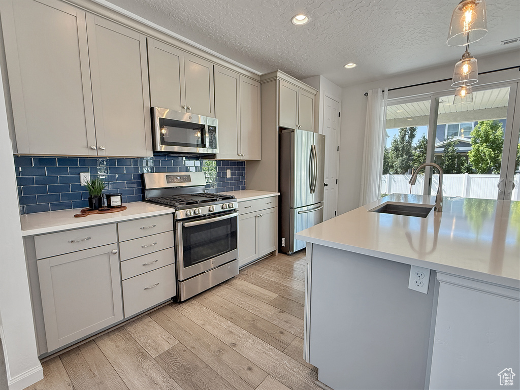 Kitchen featuring appliances with stainless steel finishes, light wood-style floors, light countertops, tasteful backsplash, and a textured ceiling