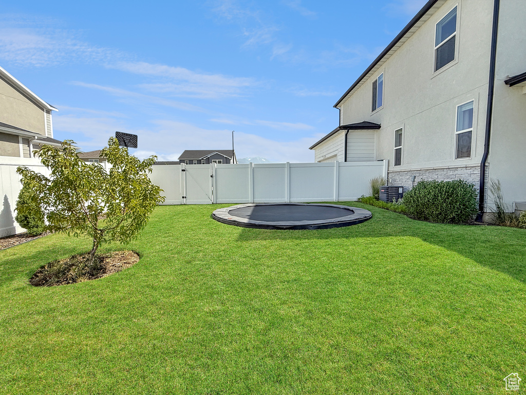 Fenced backyard featuring a trampoline and a gate