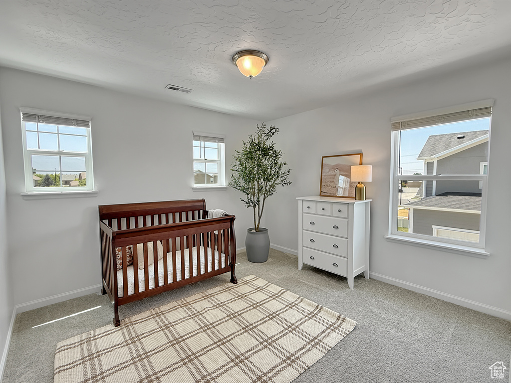 Bedroom featuring light carpet, a nursery area, and a textured ceiling