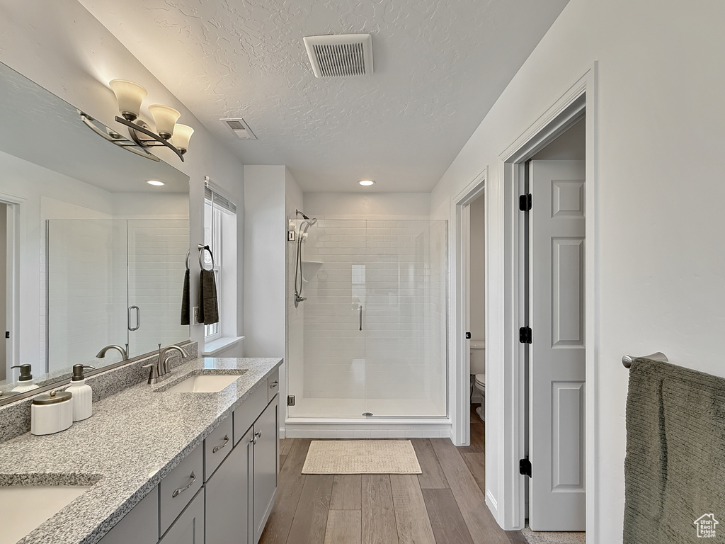 Full bathroom with wood finished floors, a stall shower, double vanity, a textured ceiling, and recessed lighting