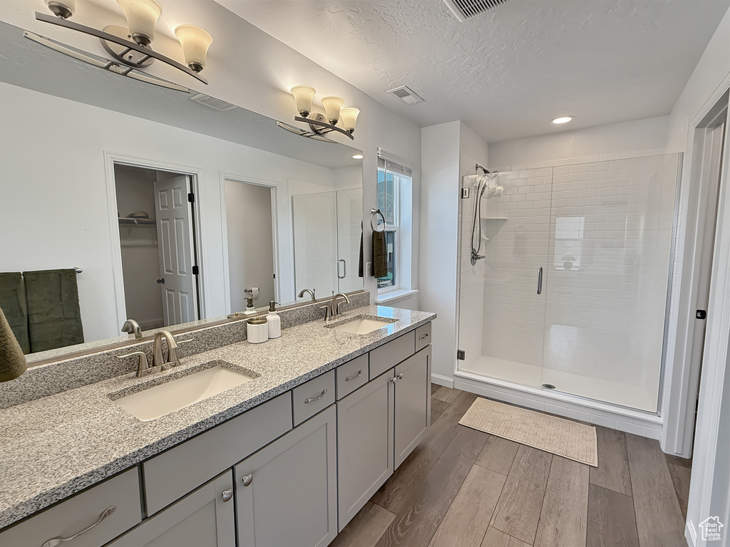 Bathroom with wood finished floors, a shower stall, double vanity, recessed lighting, and a textured ceiling