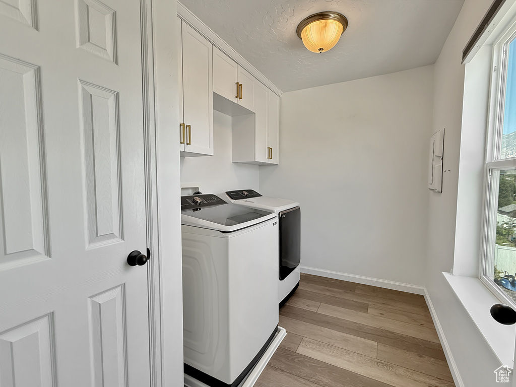 Washroom with washer and clothes dryer, cabinet space, and wood finished floors