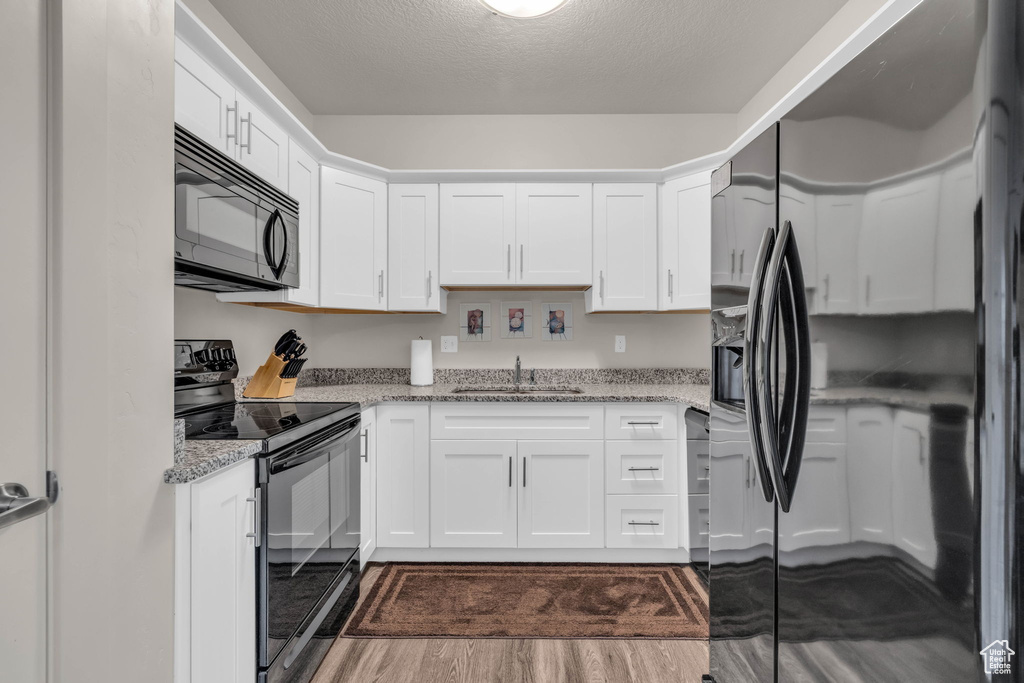 Kitchen with black appliances, white cabinets, dark wood-style flooring, and light stone counters