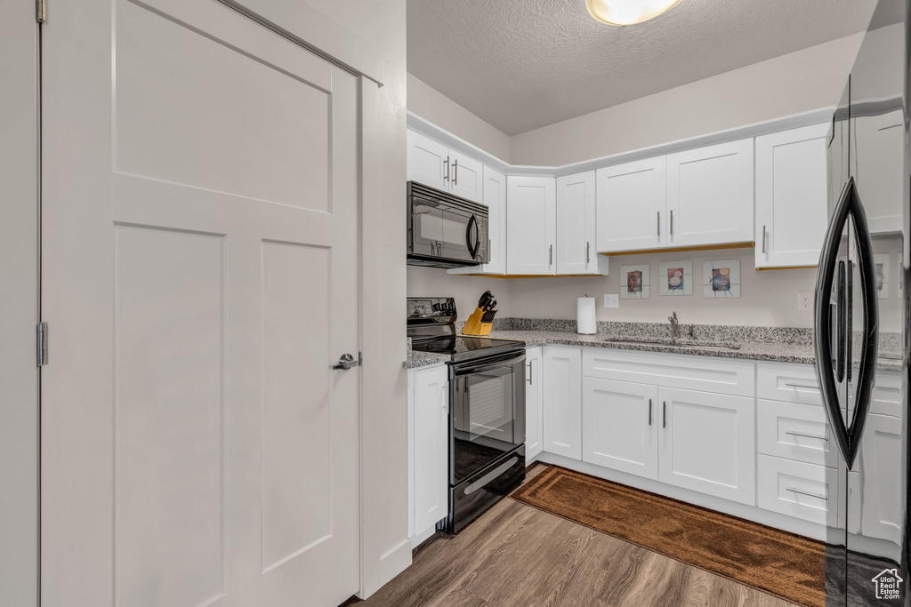 Kitchen with black appliances, dark wood finished floors, a textured ceiling, white cabinetry, and light stone counters