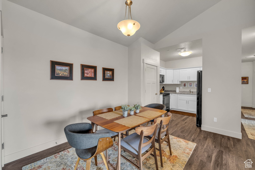 Dining area with lofted ceiling and dark wood-style floors
