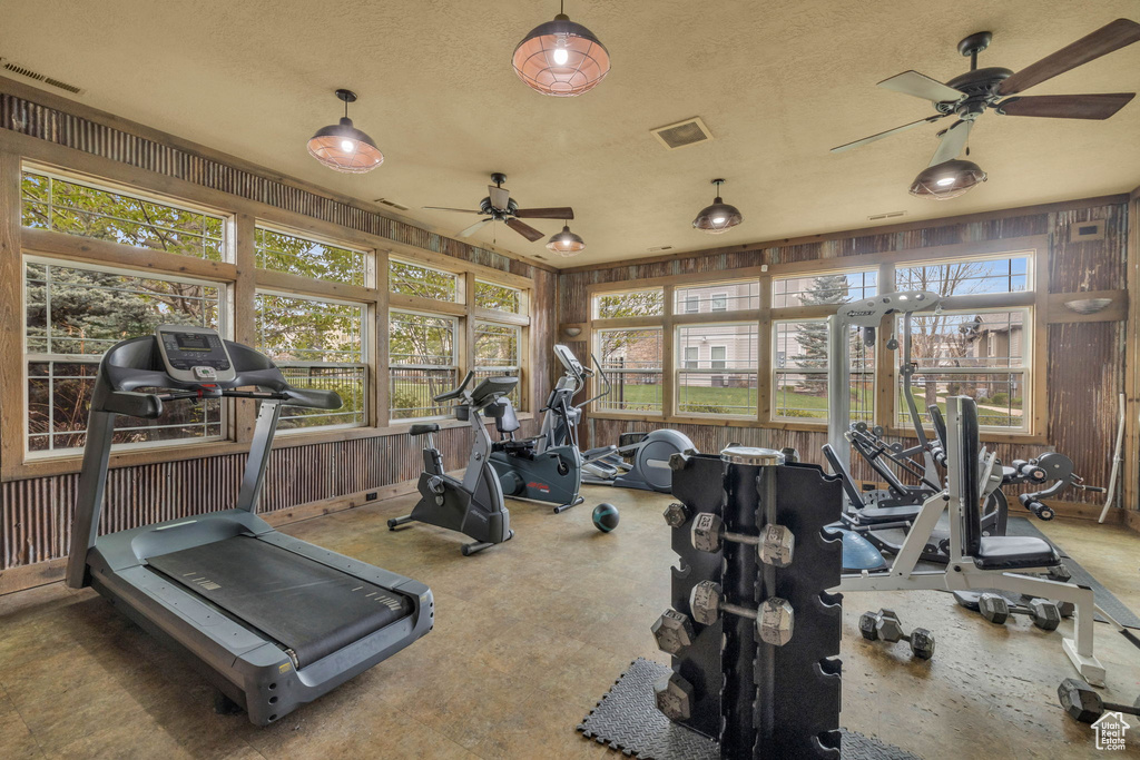 Workout area with a ceiling fan, wooden walls, and a textured ceiling