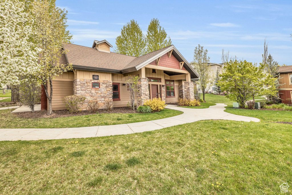 Craftsman-style home with stone siding, board and batten siding, roof with shingles, and a front yard