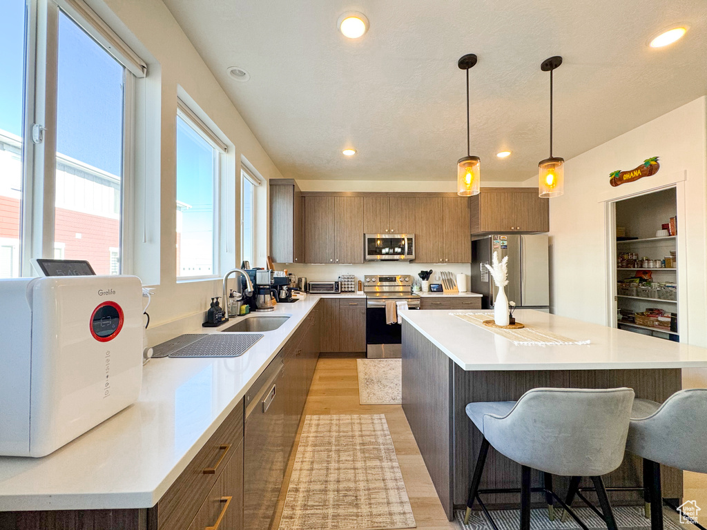 Kitchen featuring stainless steel appliances, modern cabinets, a kitchen breakfast bar, brown cabinets, and light wood-style flooring