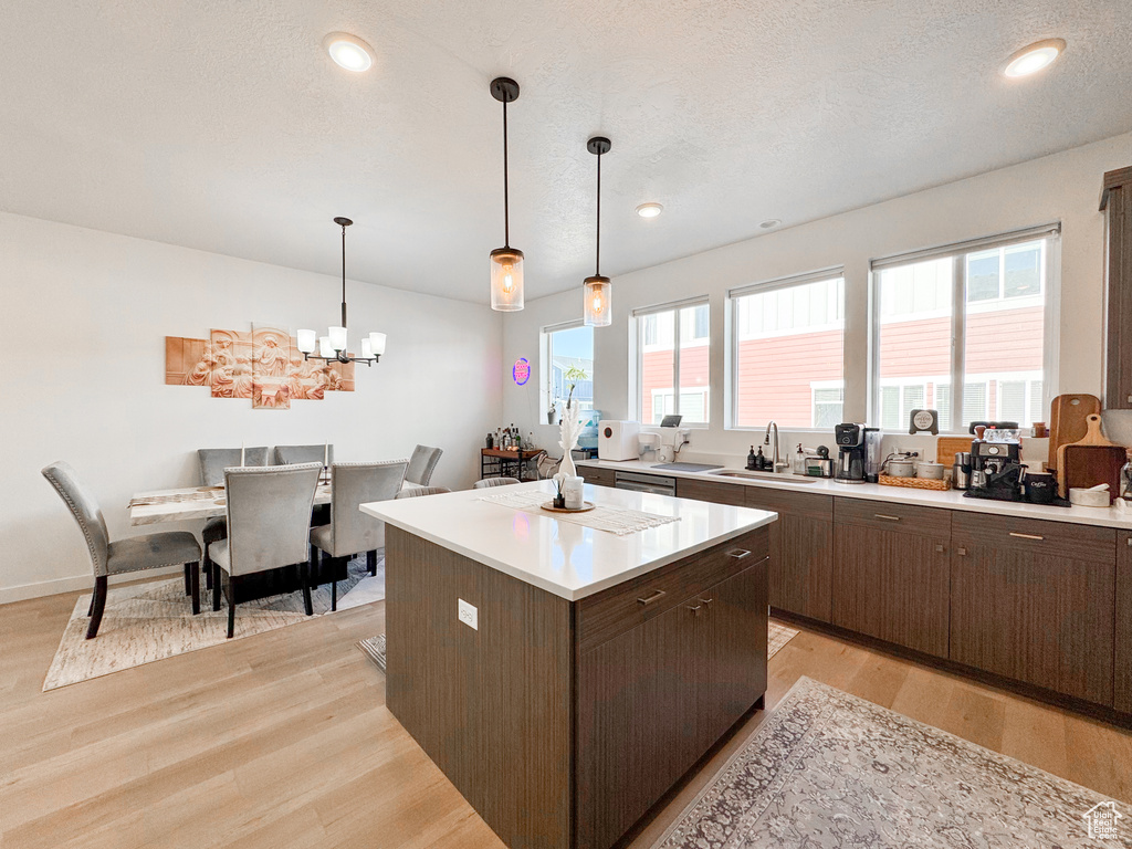 Kitchen with light wood-style flooring, light countertops, a center island, a chandelier, and stainless steel dishwasher