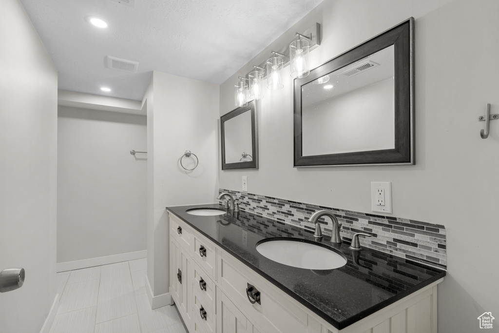 Bathroom with double vanity, decorative backsplash, and recessed lighting