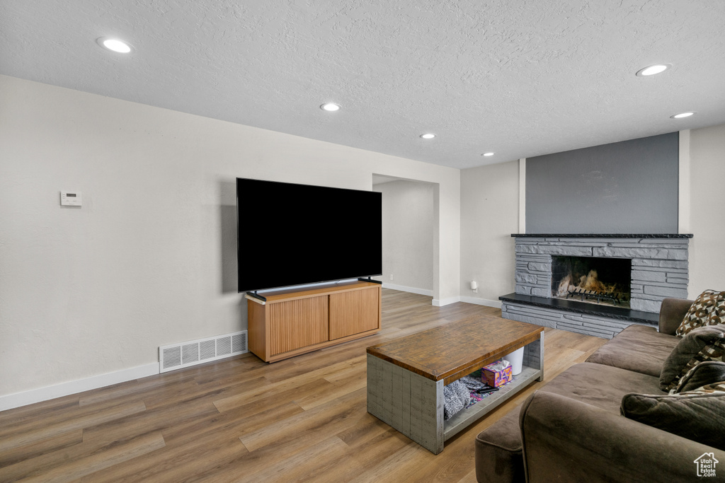 Living area with a textured ceiling, light wood-style flooring, a stone fireplace, and recessed lighting